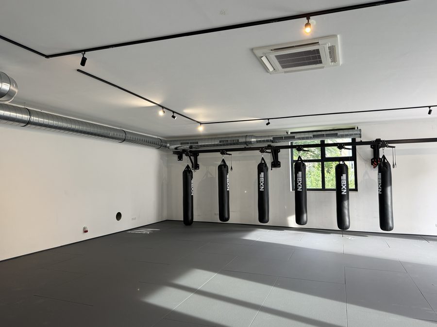 Trainingssaal mit sechs Boxsäcken an der Wandschiene, darüber Lüftungskanal und Deckenkassette