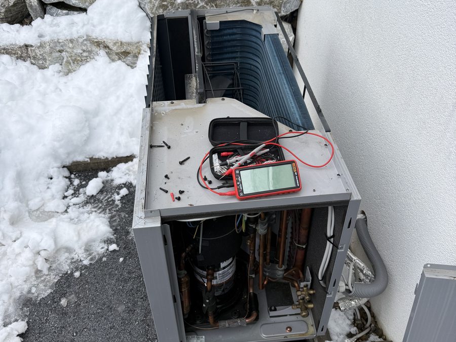 Geöffnete Wärmepumpen-Außeneinheit im Schnee, darauf ein Multimeter bei der Fehlersuche